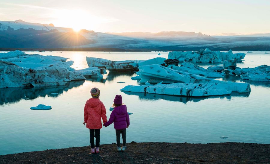 To børn ser på isbjerge, med solen i baggrunden